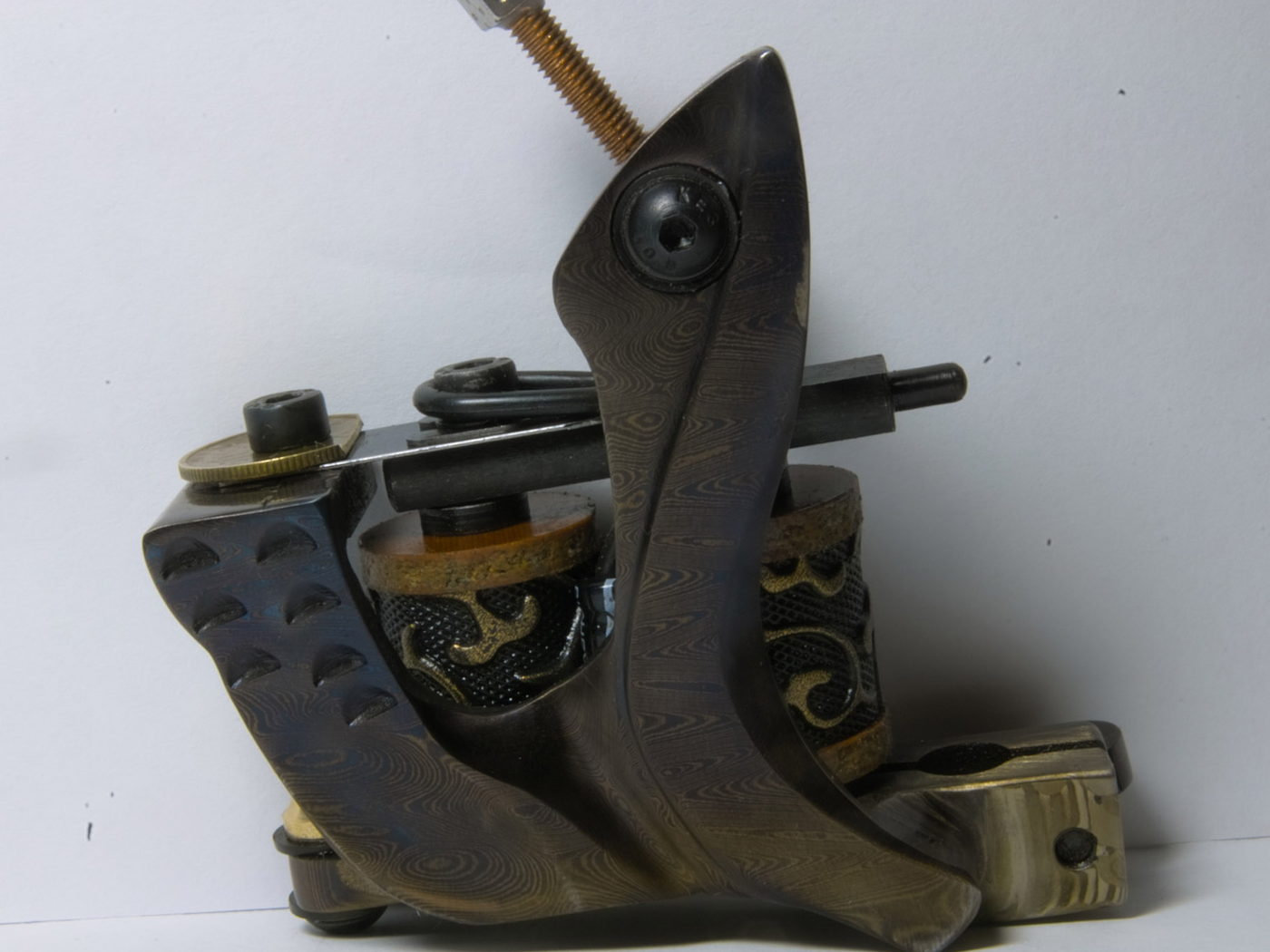 A coil tattoo machine seen in profile on a pale ground, frame, springs and contact screw all visible.