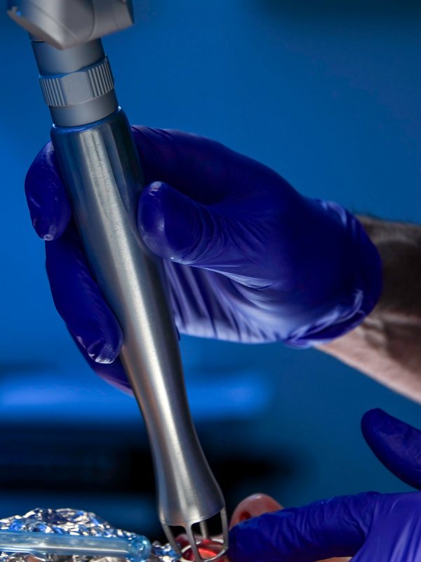 Gloved hand holding a laser handpiece against a blue background