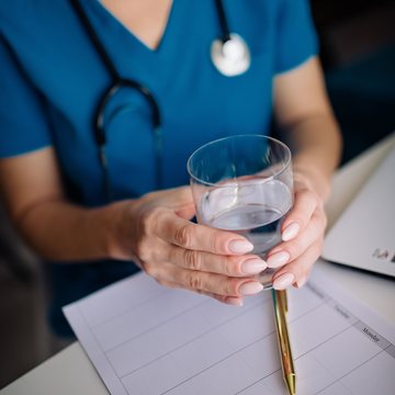 Clinician in teal scrubs holding a glass of water beside treatment notes