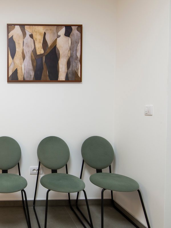 Waiting area with three green chairs below a framed artwork
