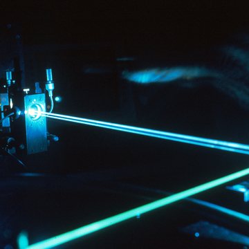 Teal laser beams crossing an optical bench in a darkened room