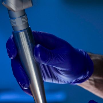 Gloved hand holding a laser handpiece against a blue background