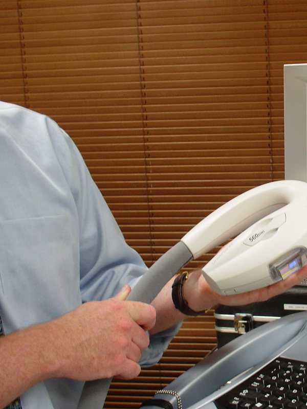 A clinician steadying a laser handpiece over the treatment head