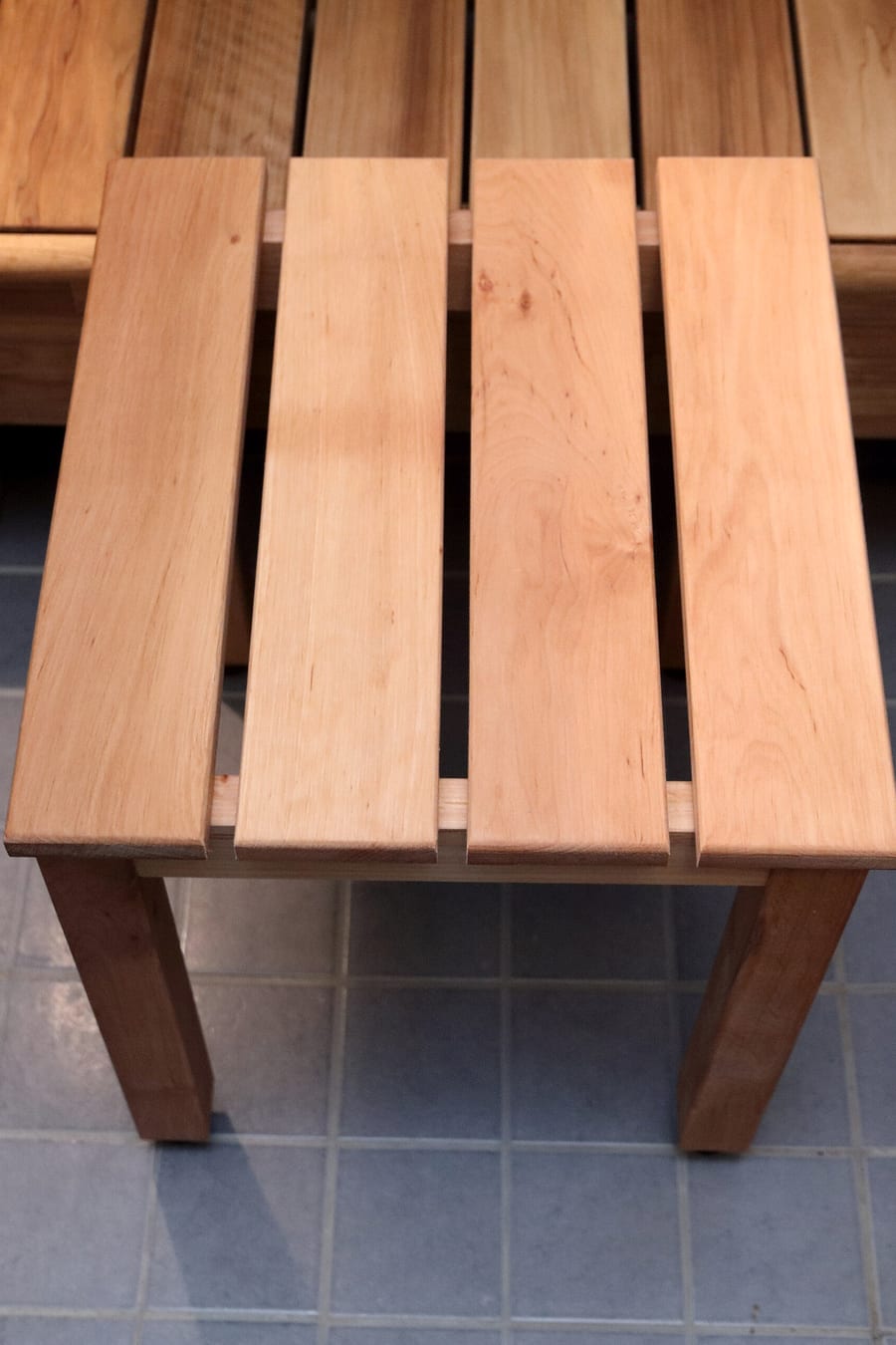 A light wooden slatted sauna stool standing on a bench over blue tiles.
