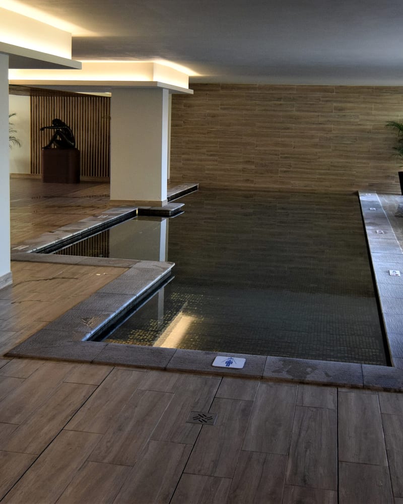 An indoor spa pool along a wood-effect wall, with a white column and a wooden deck at its edge.