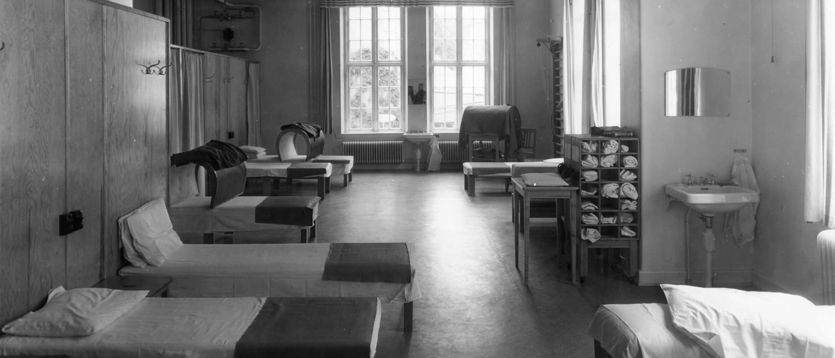 A black-and-white treatment room with made-up beds, a rack of folded towels and a sink by the window.