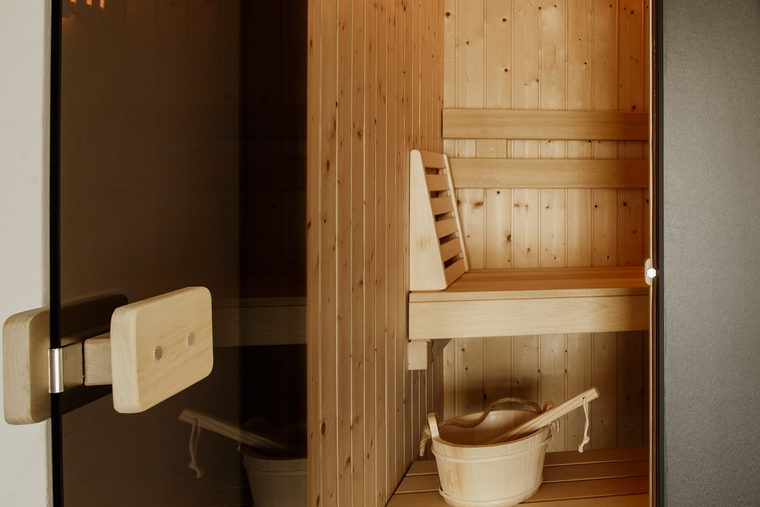A small wood-lined sauna with its door open beside a panelled wall.