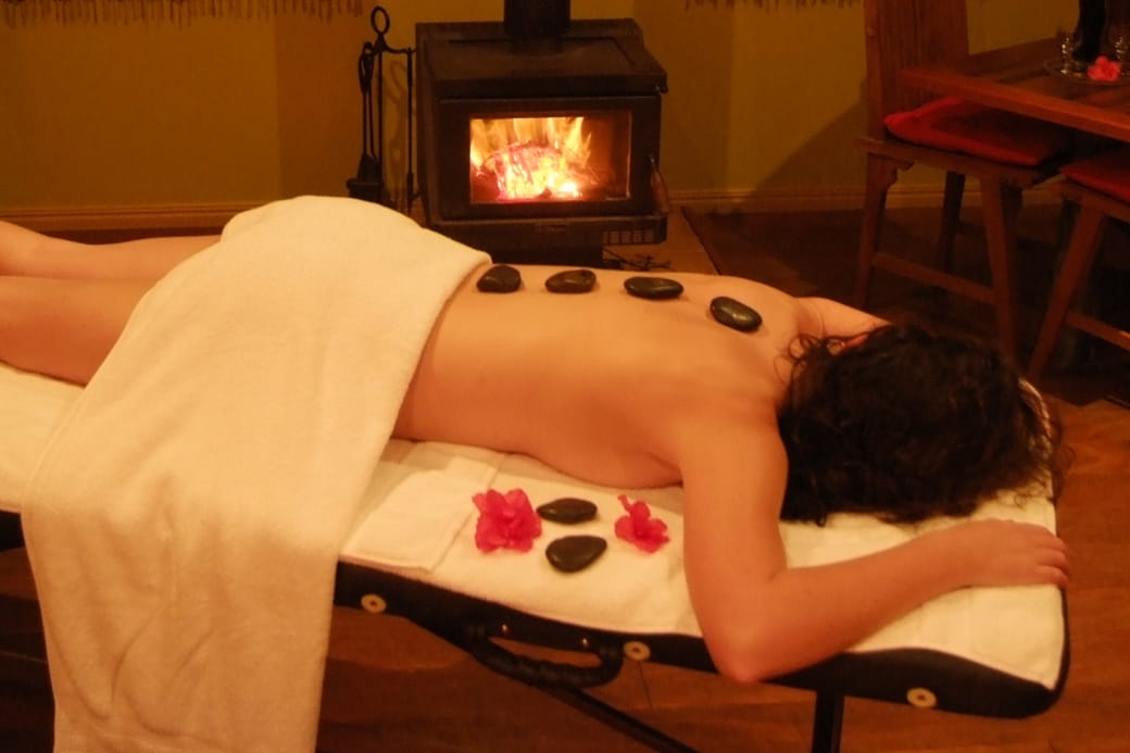 Warmed stones set in a row along a covered back on a massage table in a softly lit room.