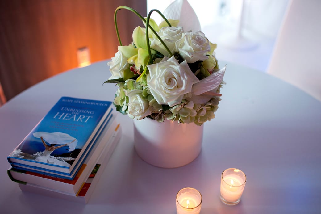 A low table in the quiet room holding white roses in a pot, a book and two lit tealights.