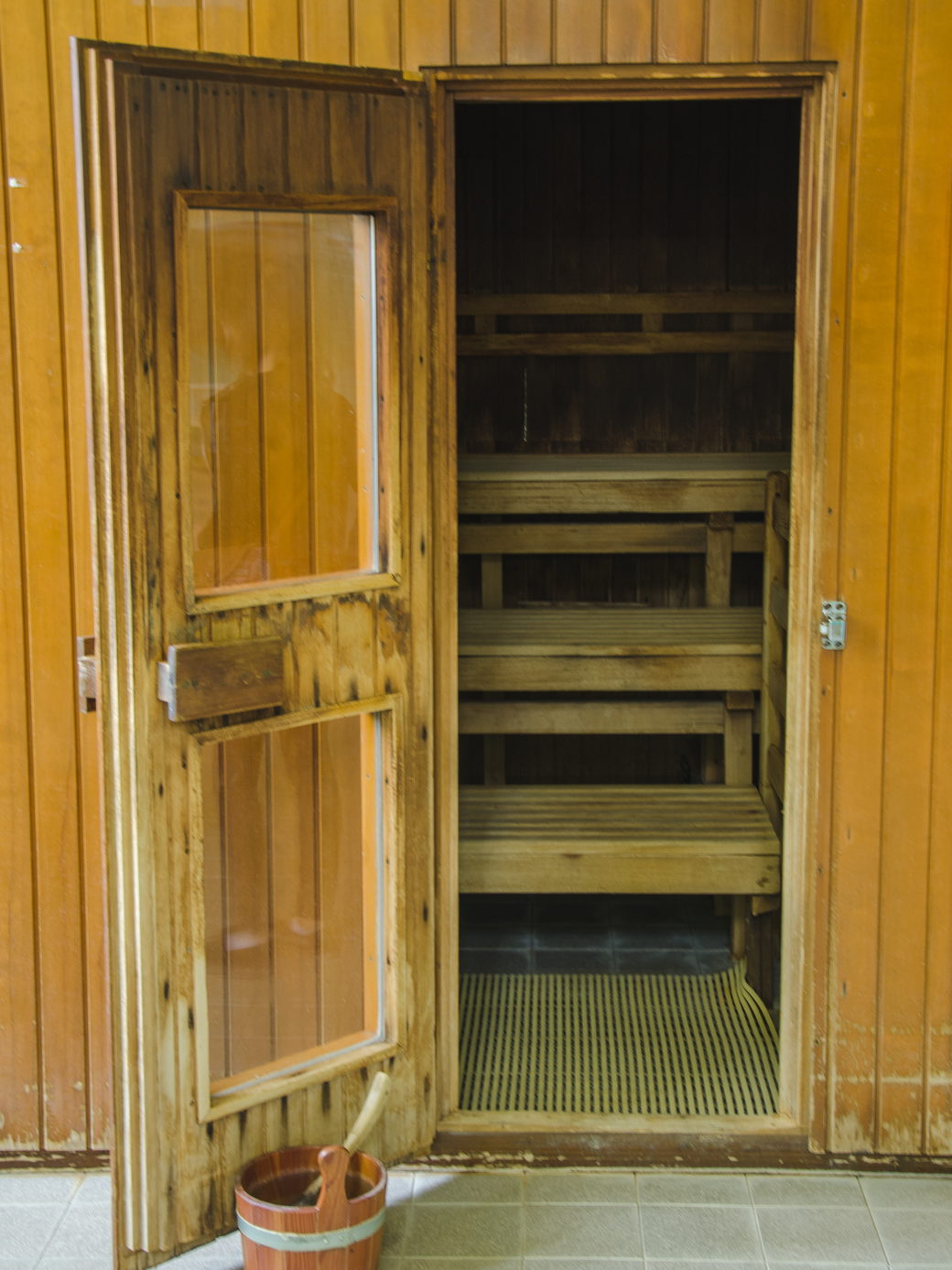 An open sauna doorway looking in on tiered timber benches and a wooden bucket.