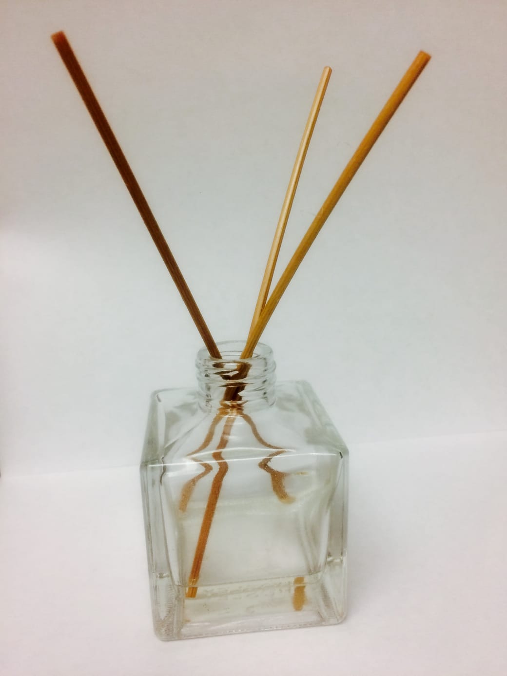 A reed diffuser on a pale surface, its sticks fanned out above the bottle.