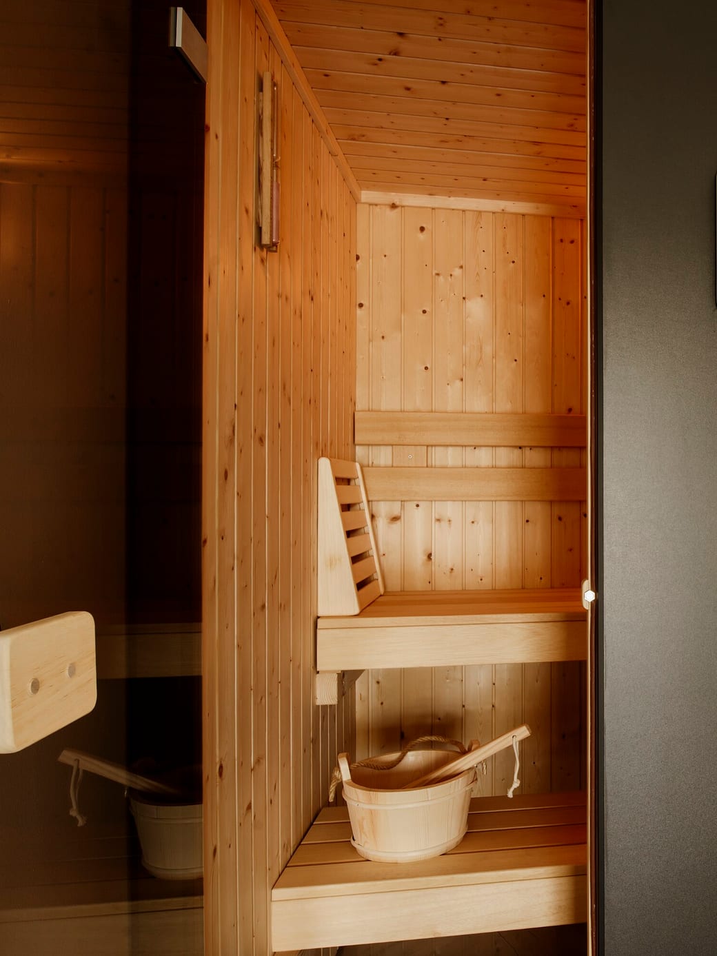 A cedar-lined sauna cabin with its bench and a wooden water bucket.