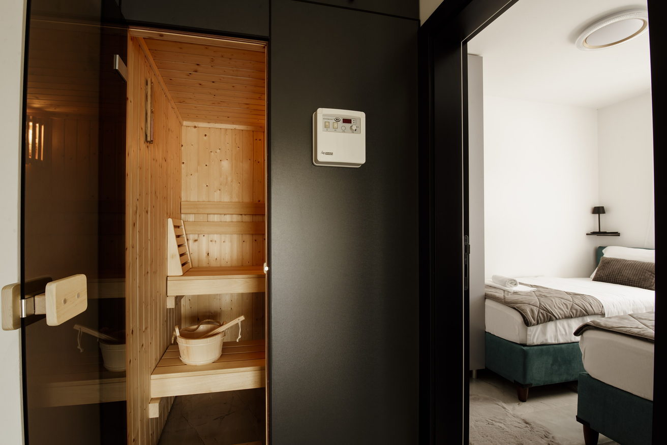 A small wood-lined sauna room with a bench, seen through its glass door from an adjoining room.