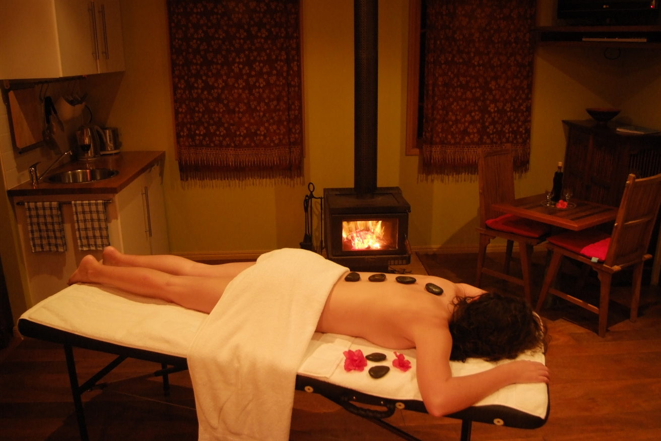 Warm stones laid along a client's back on a massage table, with a stove lit behind.