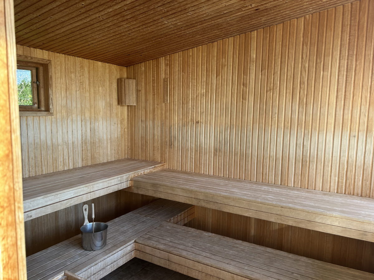 A timber-lined sauna room with a bench and a small window, empty and lit by daylight.