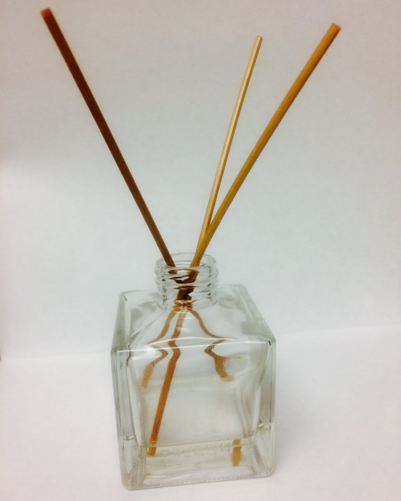 A glass reed diffuser on a plain surface, photographed from a short distance.