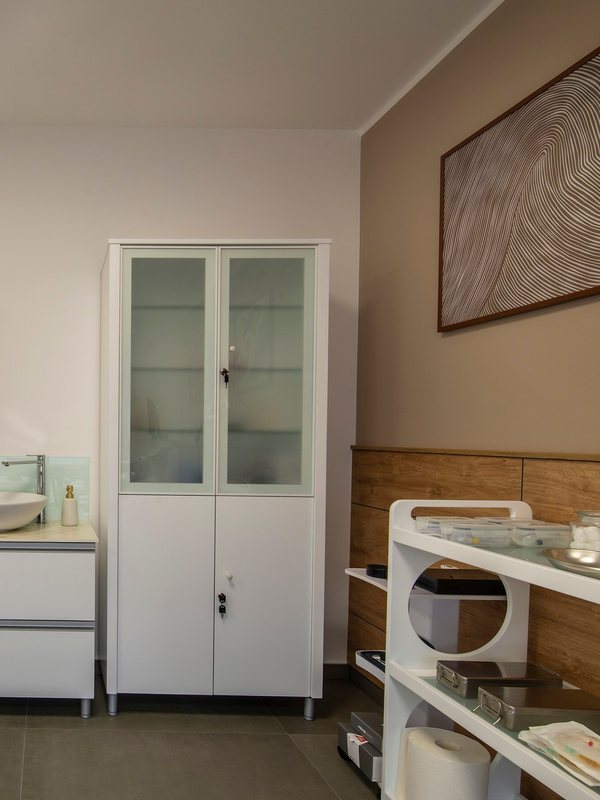 A clinic room with a washbasin and a glass-fronted supply cabinet
