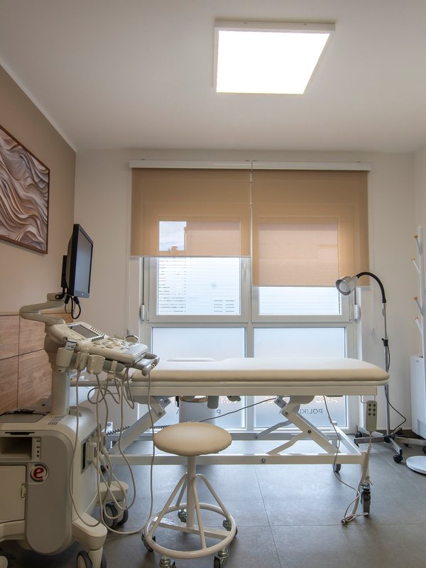 A bright examination room with a treatment couch and monitor