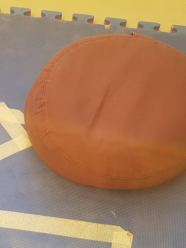 A round terracotta meditation cushion resting on a floor mat