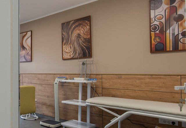 Examination couch and equipment trolley below three framed abstract prints