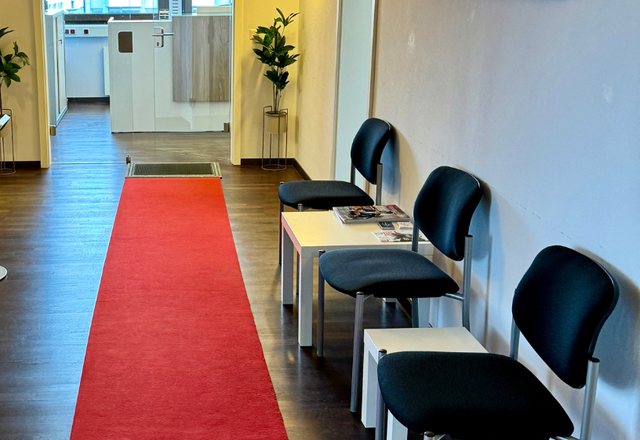 Waiting room with a red carpet runner, black chairs and magazines on a low table