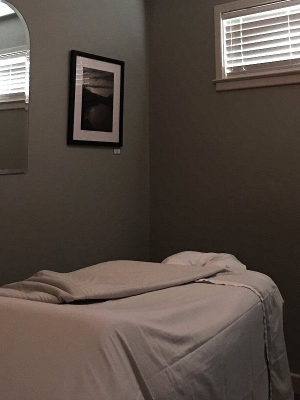 Treatment couch made up in cream linen in a softly lit room with a framed print