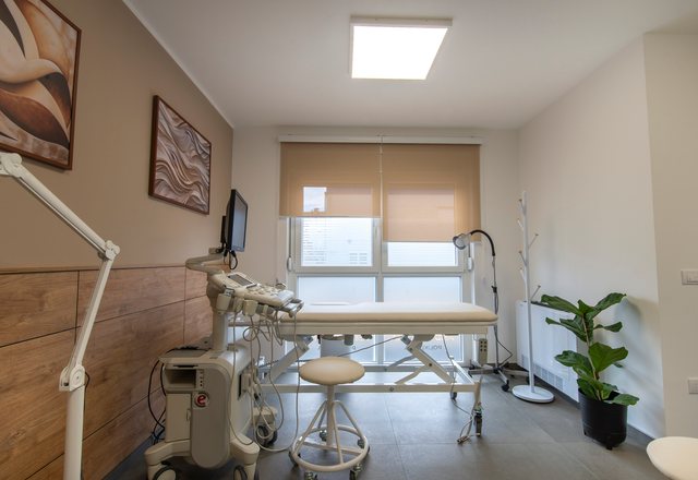 Examination couch with an adjustable lamp and a wall-mounted monitor beside a bright window