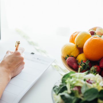 Writing a nutrition plan in a notebook beside a bowl of fresh fruit