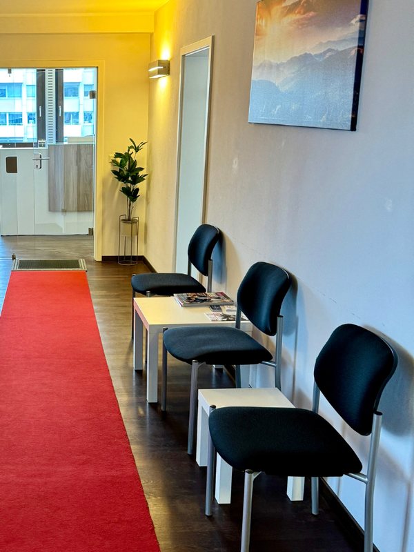 Waiting room with a red carpet runner, black chairs and a framed seascape