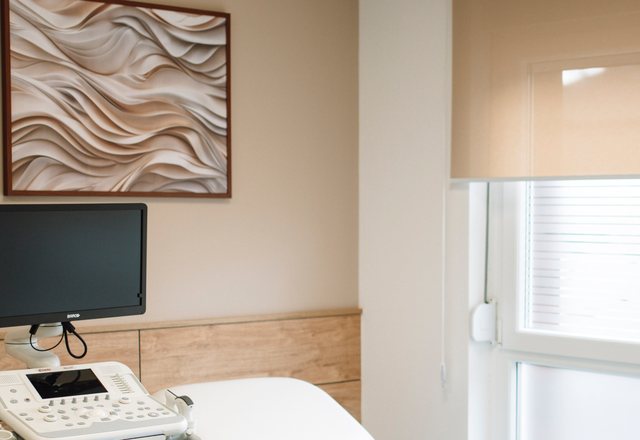 Framed textured artwork above an ultrasound console and a wall monitor