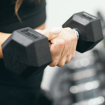 Coach Esi Mensah gripping a hex dumbbell at the top of a curl