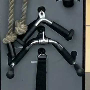 The cable-attachment board in the barbell room: a rope, a V-bar, a triangle bar and a strap handle on their hooks