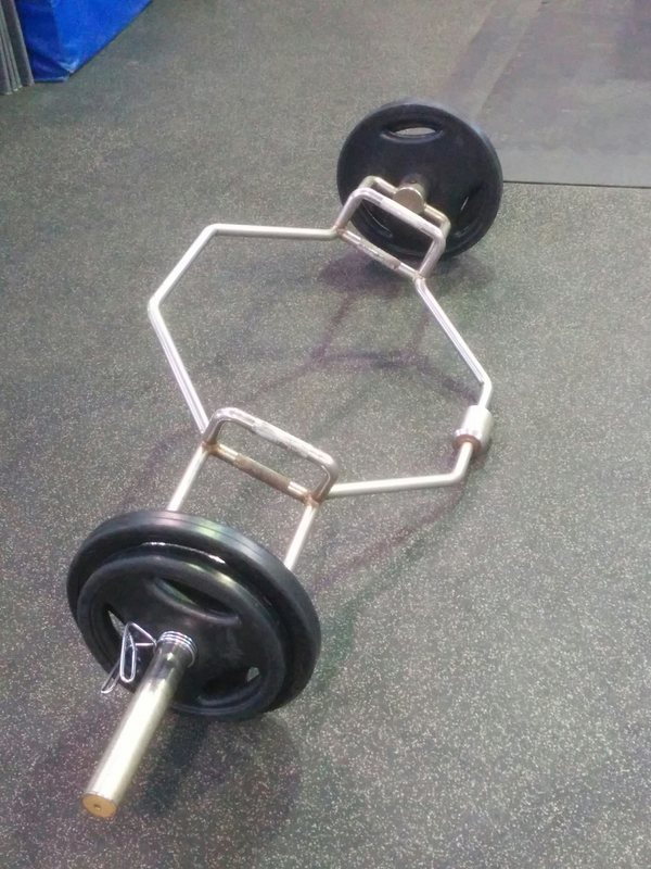 A loaded trap bar resting on the rubber floor beside its plates
