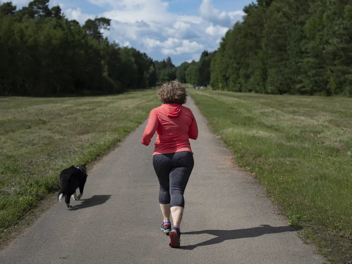 Runner and dog on a paved trail between the trees
