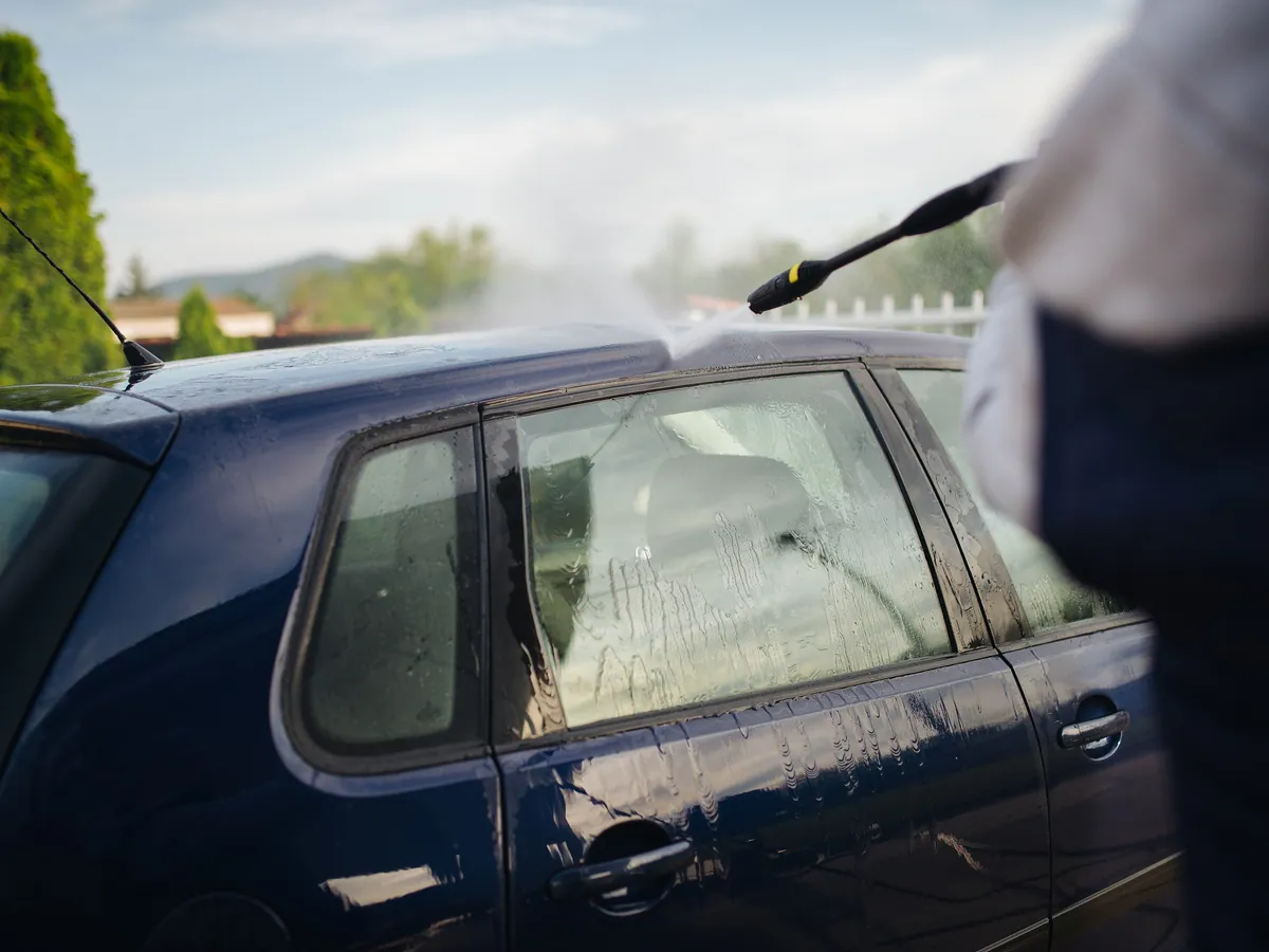 Pressure lance rinsing a blue hatchback during an exterior wash