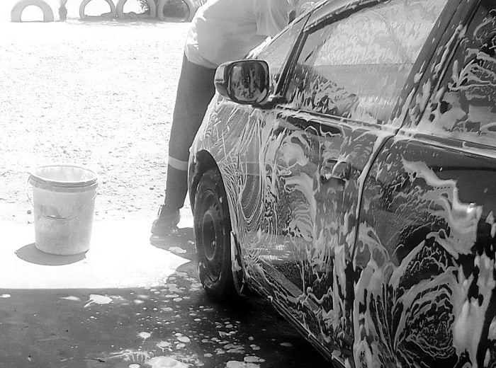 A car lathered in shampoo on a wash slab, foam running to the drain