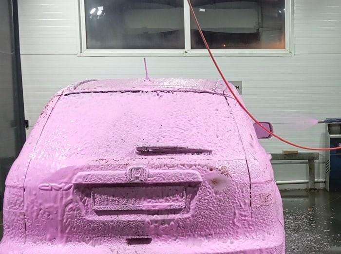 An estate car under a coat of coloured snow foam in a wash box
