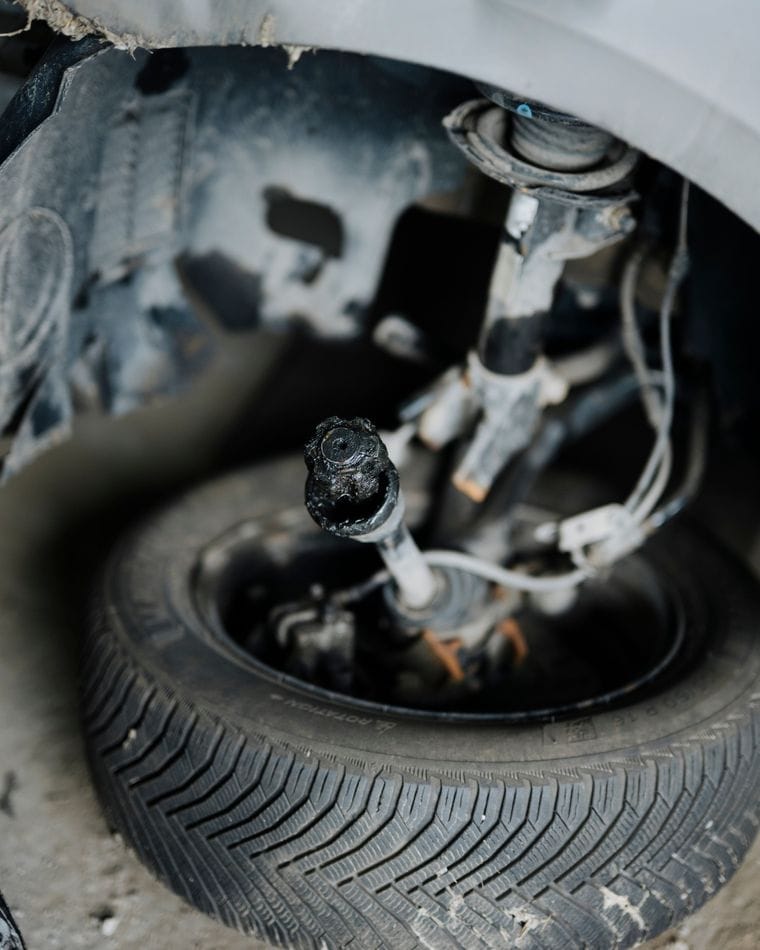 A car's front wheel and suspension, with visible damage to the suspension parts and the tire.