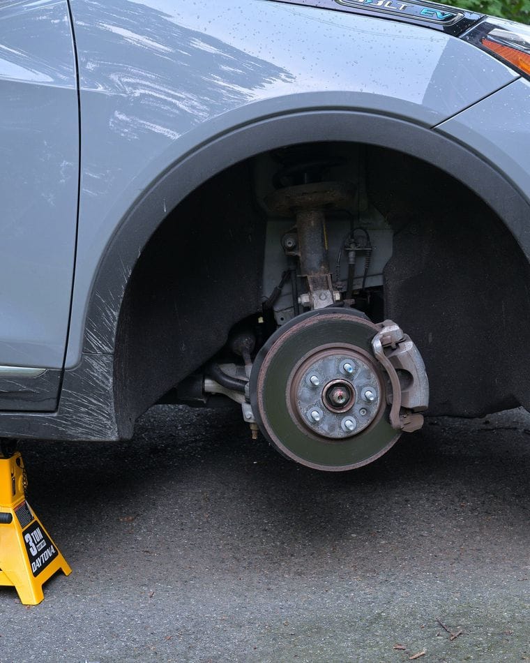 A front disc brake with the wheel removed and the car supported on a jack stand.