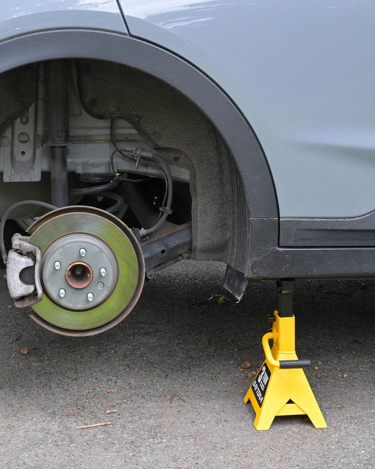 A rear disc brake and rotor with the wheel removed, the car resting on a jack stand.