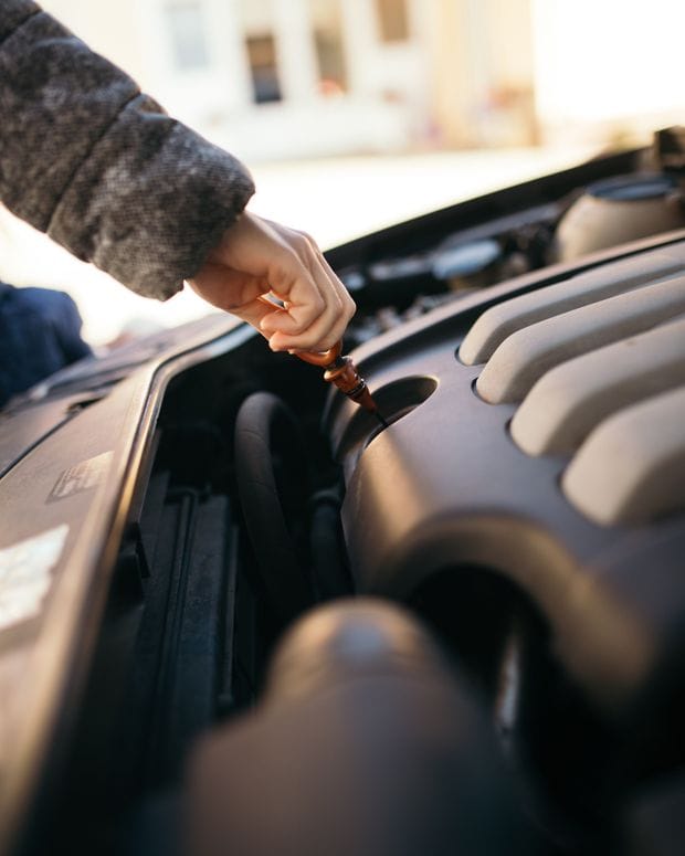 A hand drawing the engine oil dipstick from an open engine bay to check the oil level.