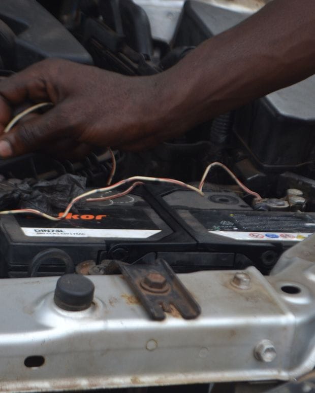 Hands working on the cable connections of a car battery inside an open engine bay.