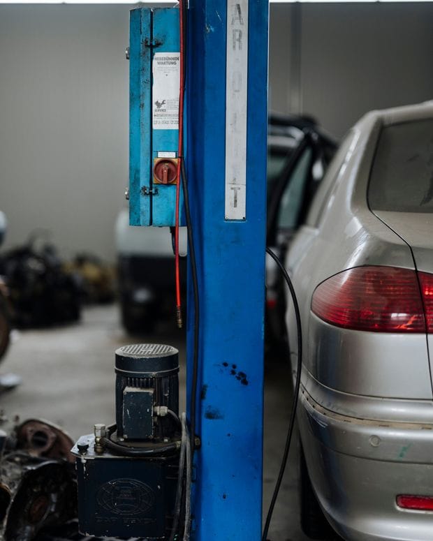 The blue column of a two-post vehicle lift in a repair shop, with a silver car parked beside it.