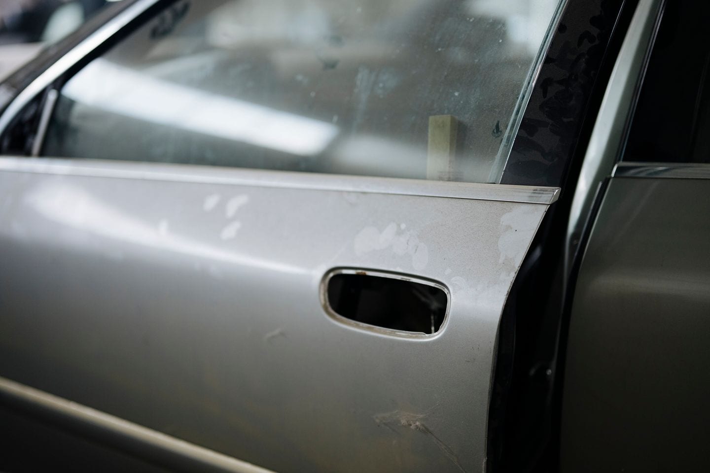 A silver car door showing wear and surface damage part-way through restoration work.