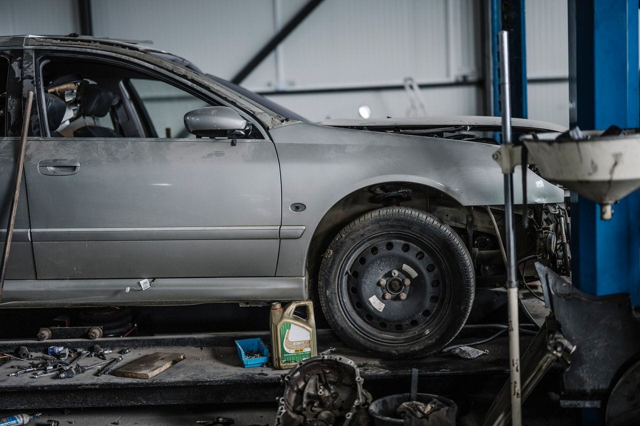 A car raised on a workshop ramp with its front end opened up, tools and equipment around the bay