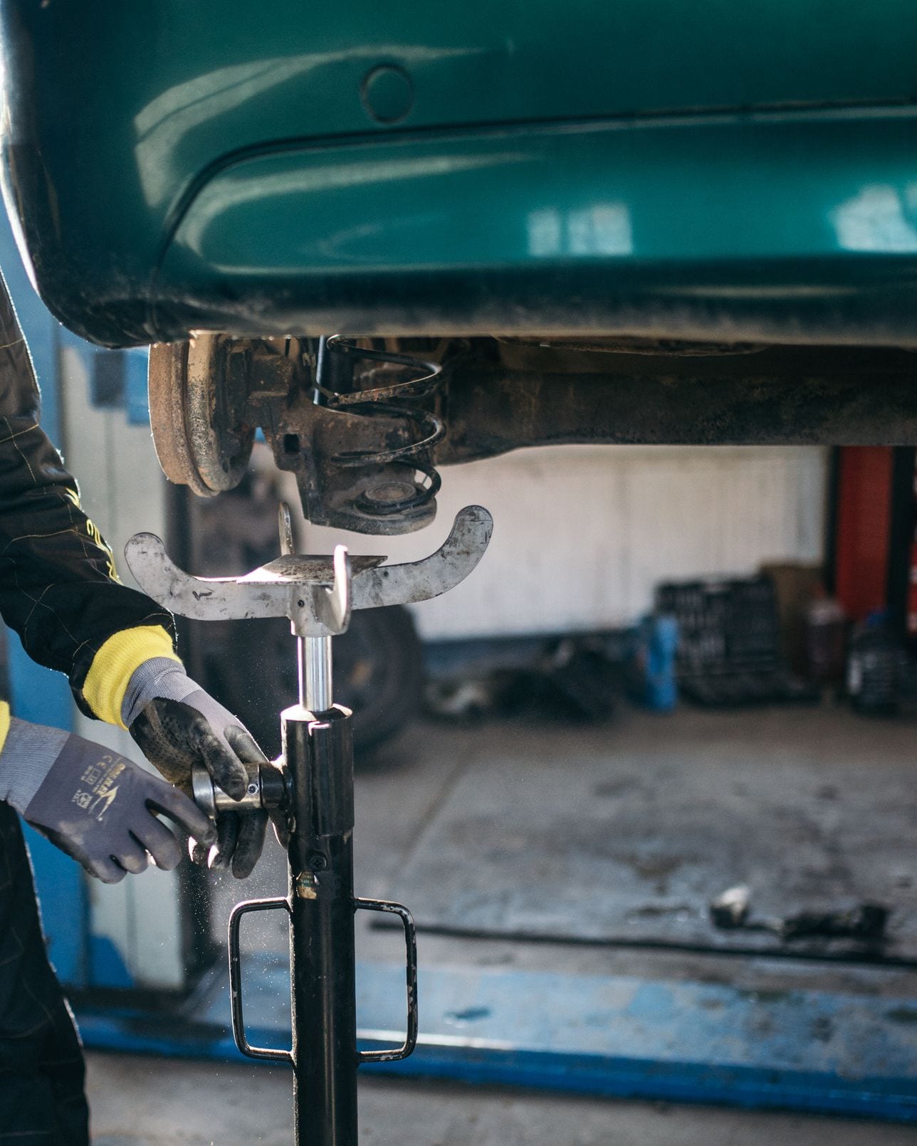 A technician in overalls working on the suspension of a car raised on a workshop lift.