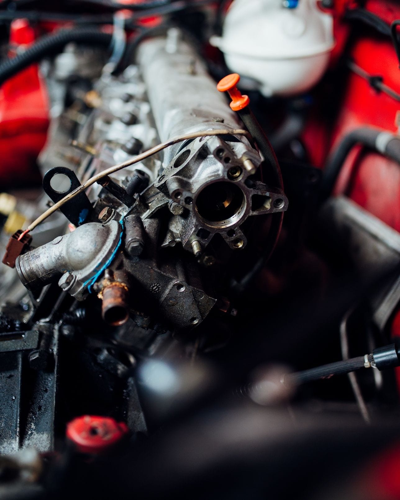 Engine components laid out in the bay of a red car during a mechanical inspection.