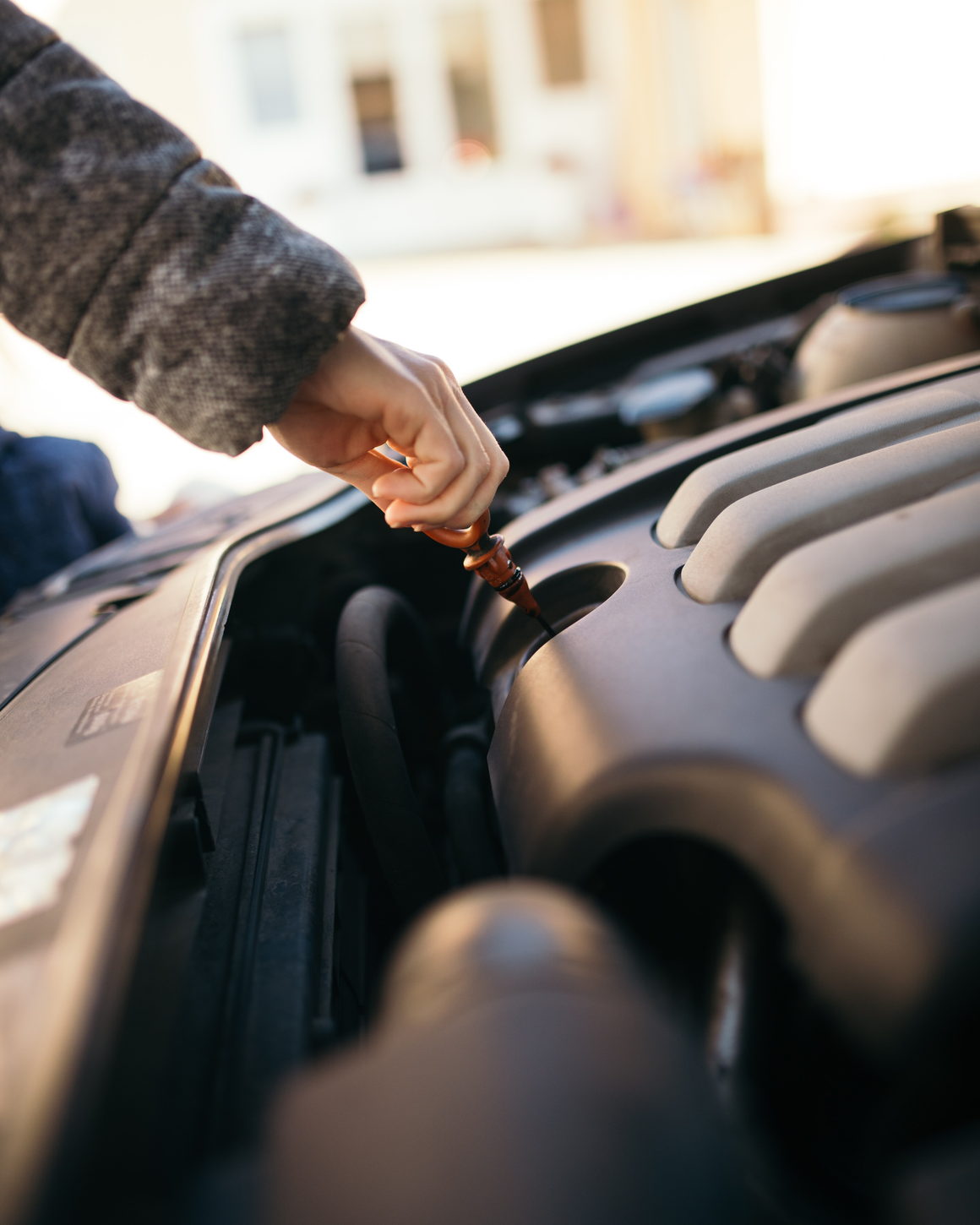 Hands drawing the dipstick from an engine at an open bonnet.