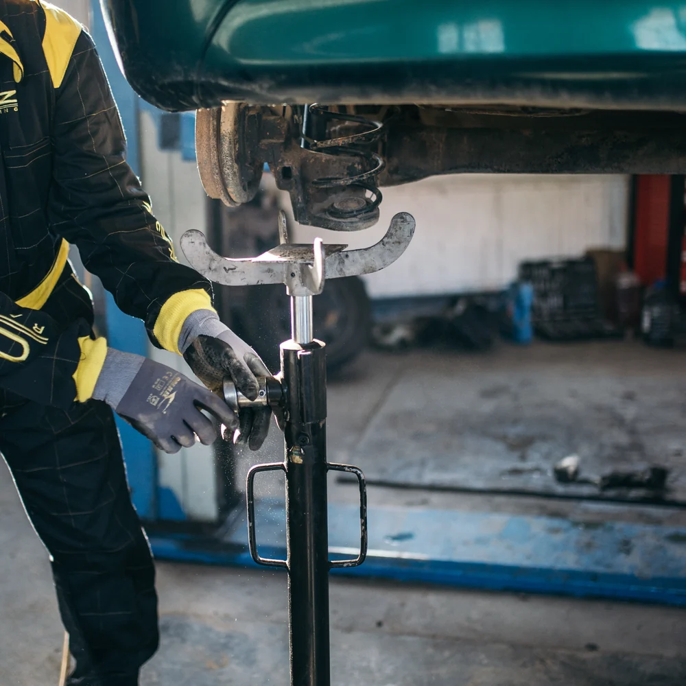 A technician working on suspension components under a lifted car