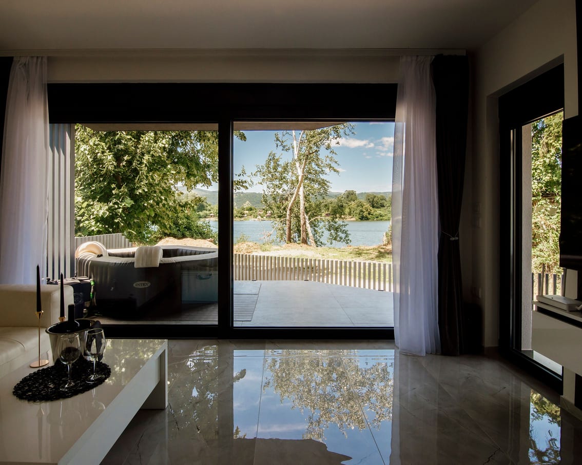 A modern living room with large windows looking out over trees and a lake.